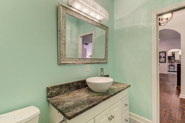 half bathroom featuring toilet, baseboards, wood finished floors, and vanity