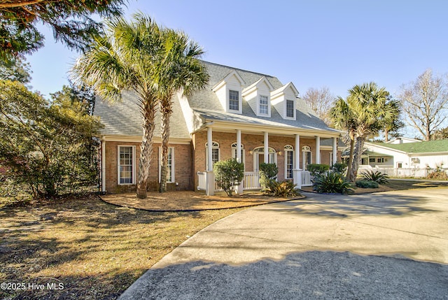 cape cod home featuring a porch, brick siding, driveway, and roof with shingles