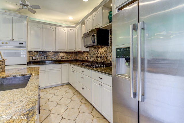 kitchen with white oven, white cabinetry, dark stone countertops, black microwave, and high end refrigerator