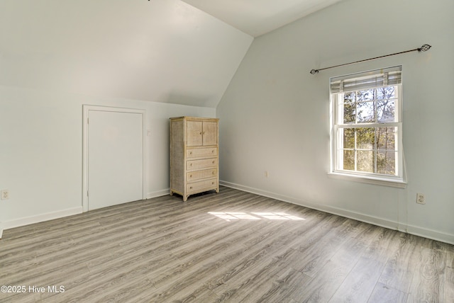 unfurnished bedroom featuring light wood-style floors, baseboards, and vaulted ceiling