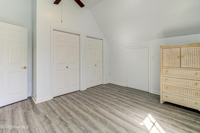 unfurnished bedroom featuring baseboards, vaulted ceiling, two closets, and wood finished floors