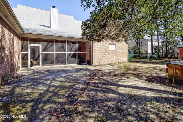 rear view of house with a patio, brick siding, fence, a sunroom, and a chimney