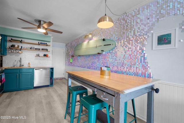 kitchen with light wood-style floors, a wainscoted wall, crown molding, and stainless steel dishwasher