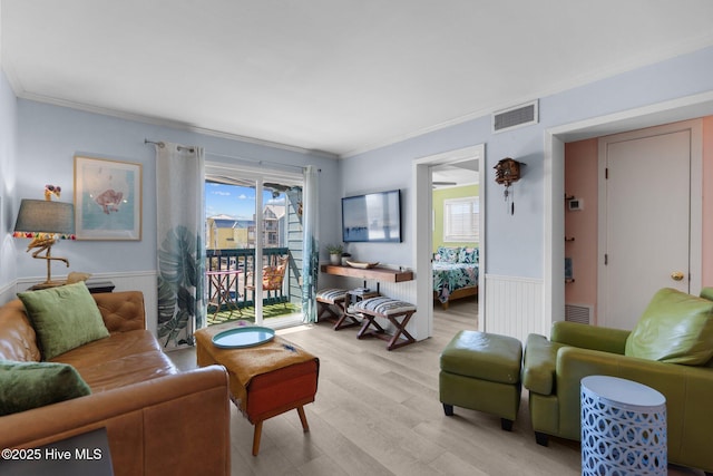 living area with ornamental molding, light wood-type flooring, wainscoting, and visible vents