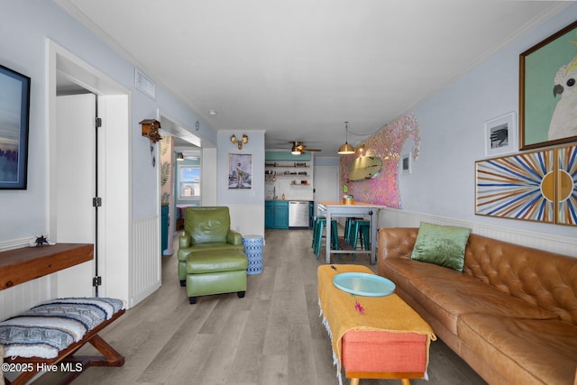 living area featuring light wood-type flooring, a wainscoted wall, crown molding, and visible vents