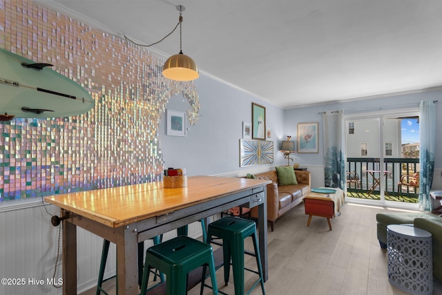 dining space featuring ornamental molding, wainscoting, and light wood-style flooring