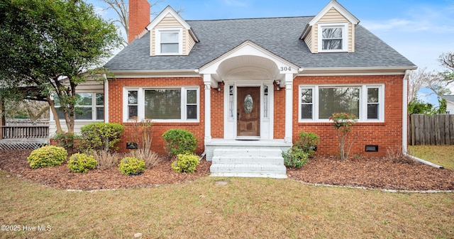 cape cod home with brick siding, a shingled roof, a chimney, crawl space, and a front yard