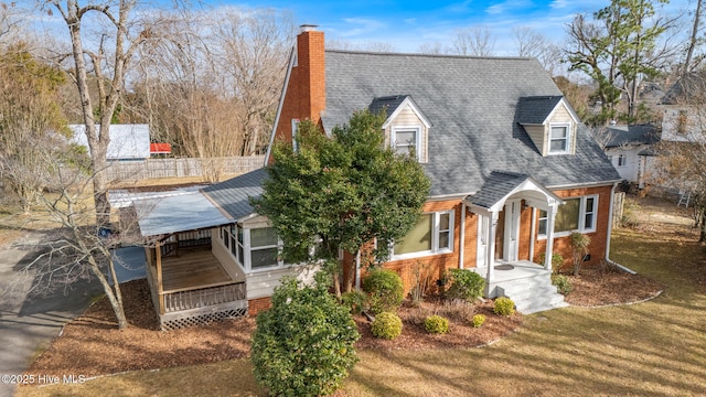 cape cod home with a shingled roof, a front yard, brick siding, and a chimney