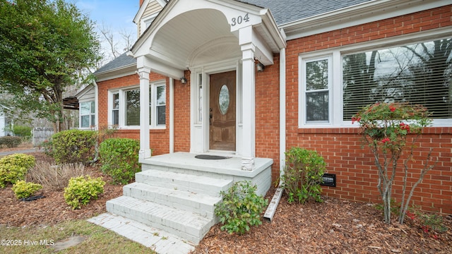 view of exterior entry with brick siding, crawl space, and a shingled roof