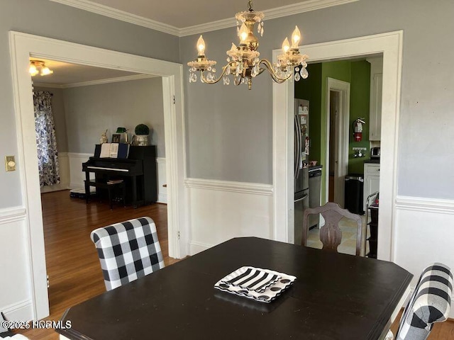 dining area featuring ornamental molding, wainscoting, an inviting chandelier, and wood finished floors