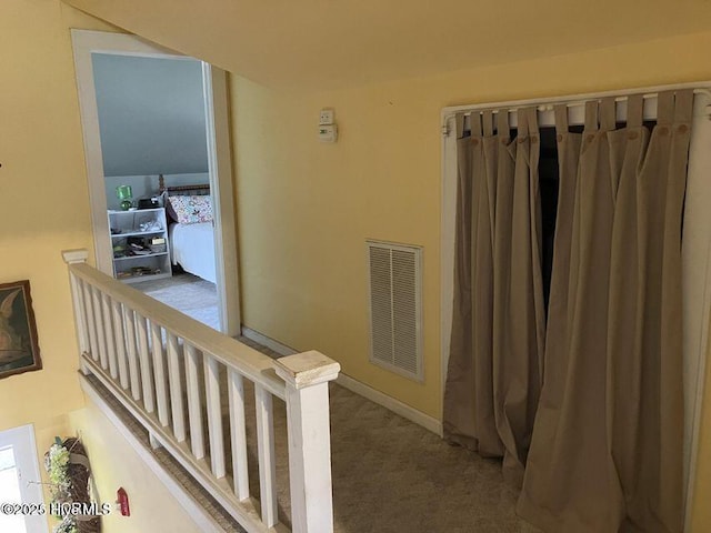 hall with carpet, an upstairs landing, and visible vents