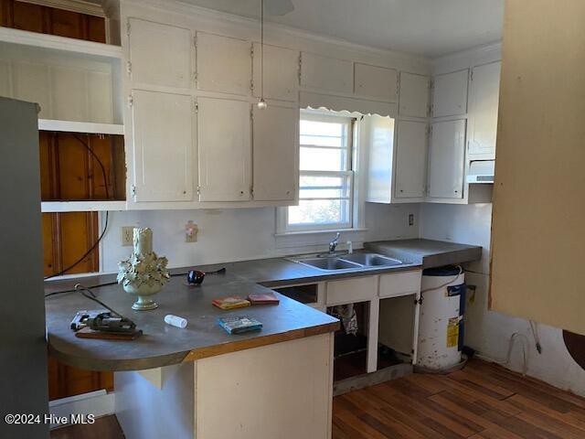 kitchen with a breakfast bar area, a peninsula, a sink, white cabinets, and dark wood finished floors