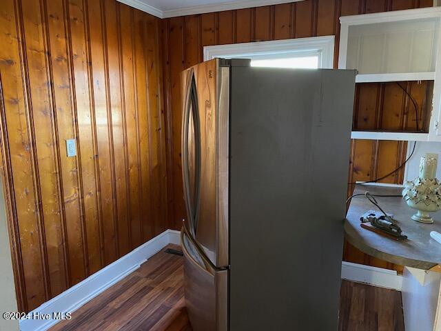 kitchen with dark wood-style floors, ornamental molding, wood walls, and freestanding refrigerator