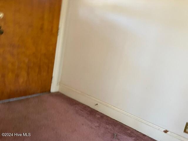 spare room featuring baseboards and dark carpet