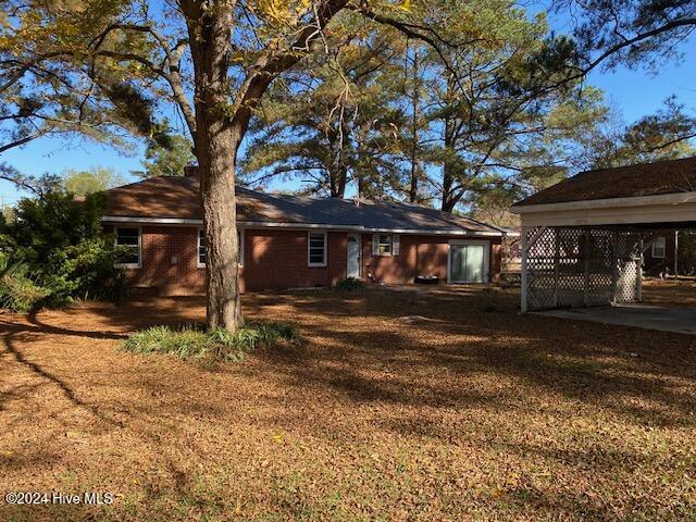 back of property with a carport, a lawn, and brick siding