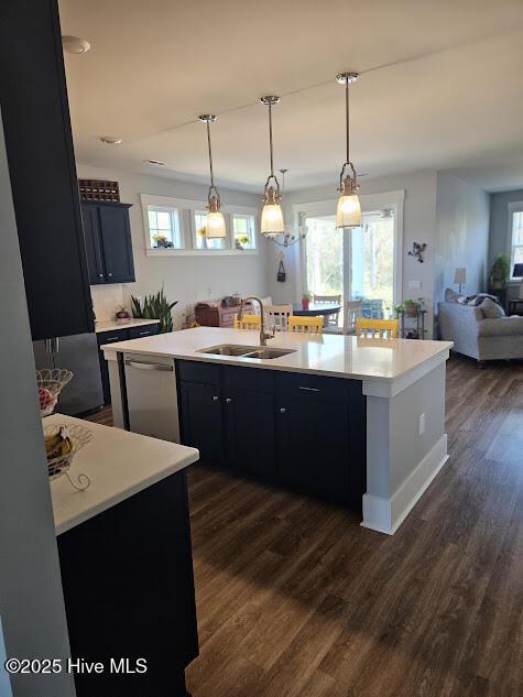 kitchen with light countertops, open floor plan, a kitchen island with sink, a sink, and dishwasher