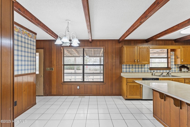 kitchen with a textured ceiling, a sink, light countertops, stainless steel dishwasher, and beamed ceiling