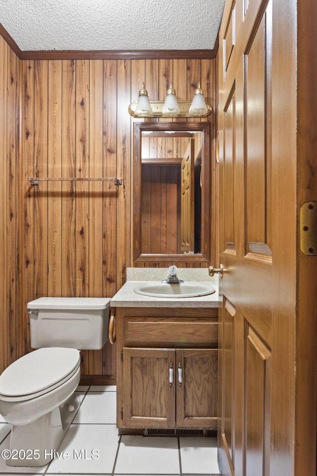 half bathroom with toilet, tile patterned flooring, a textured ceiling, vanity, and wood walls