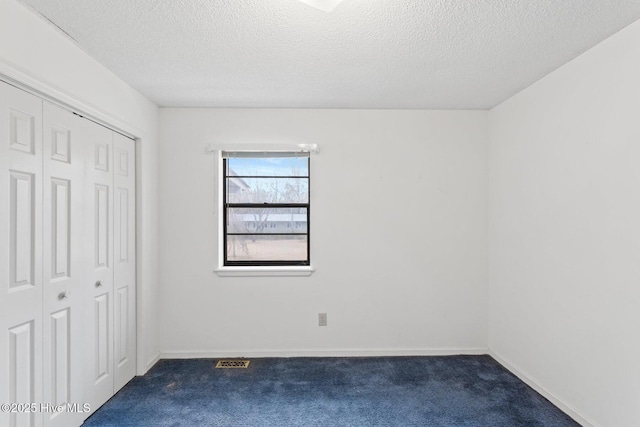 unfurnished bedroom with a closet, dark carpet, a textured ceiling, and baseboards