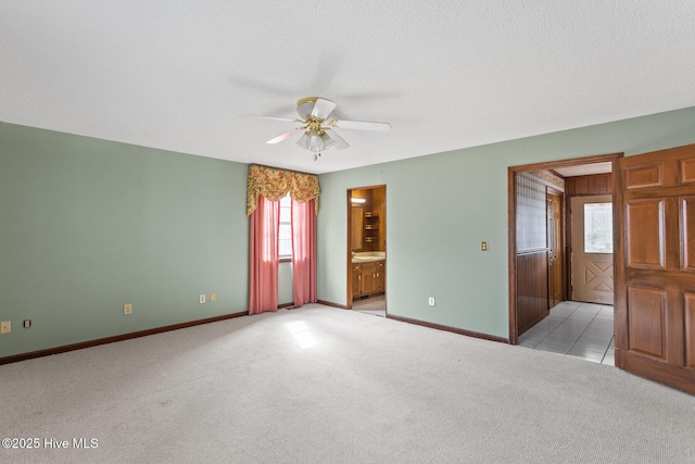 unfurnished bedroom featuring light carpet, baseboards, ensuite bath, ceiling fan, and a textured ceiling