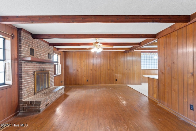 unfurnished living room with a fireplace, wooden walls, hardwood / wood-style floors, and a textured ceiling