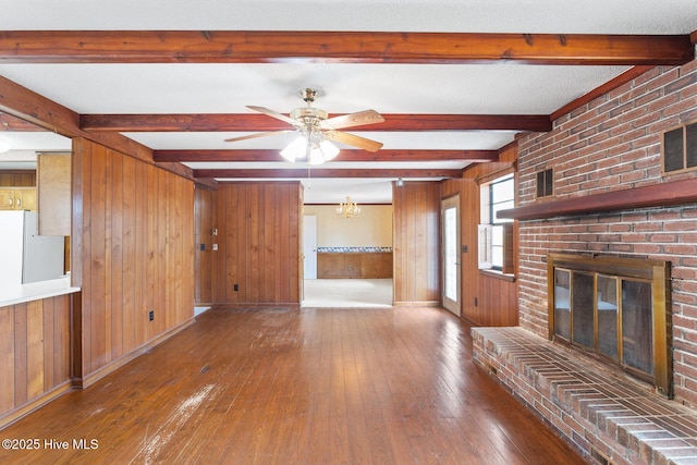 unfurnished living room with a brick fireplace, wood-type flooring, wooden walls, and beam ceiling