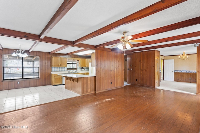 interior space featuring light wood-style floors, beamed ceiling, wooden walls, and ceiling fan with notable chandelier