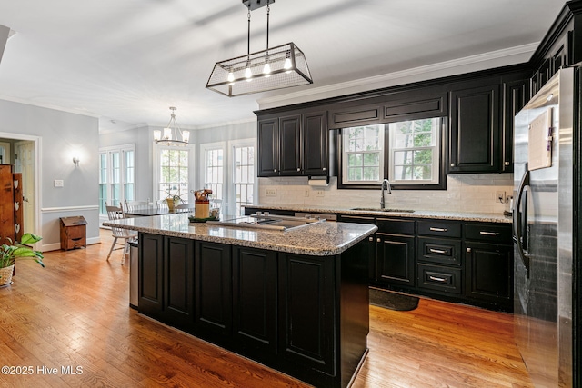 kitchen featuring a sink, cooktop, freestanding refrigerator, and dark cabinets