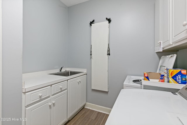laundry area featuring cabinet space, a sink, separate washer and dryer, baseboards, and wood finished floors