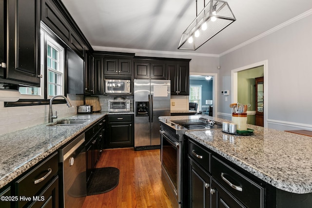 kitchen featuring a kitchen island, crown molding, a sink, dark cabinets, and stainless steel appliances