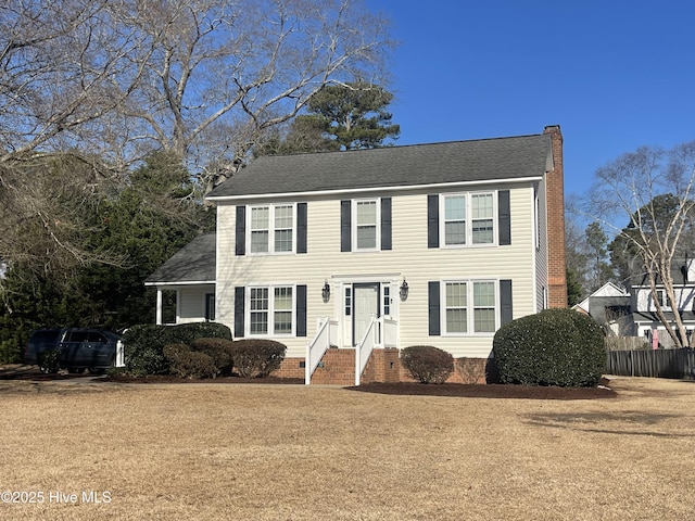 colonial-style house featuring a shingled roof, a front yard, and a chimney