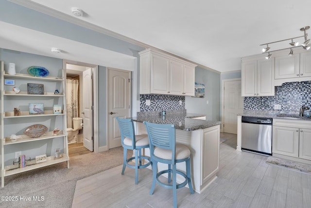 kitchen featuring white cabinets, dishwasher, ornamental molding, a kitchen breakfast bar, and a sink