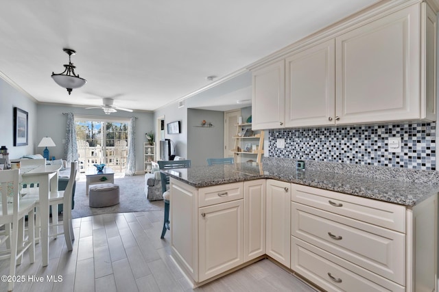 kitchen with open floor plan, a peninsula, stone counters, and backsplash