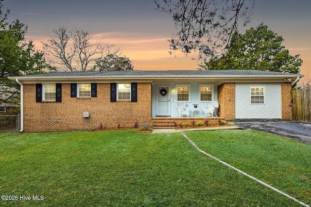 ranch-style home with a porch, fence, a front lawn, and brick siding