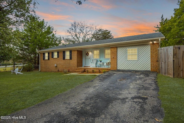 single story home with covered porch, brick siding, fence, driveway, and a front yard