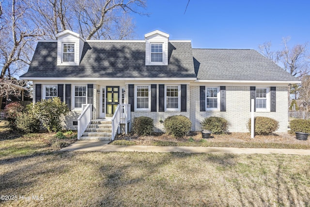 view of front of house with roof with shingles, brick siding, and a front lawn