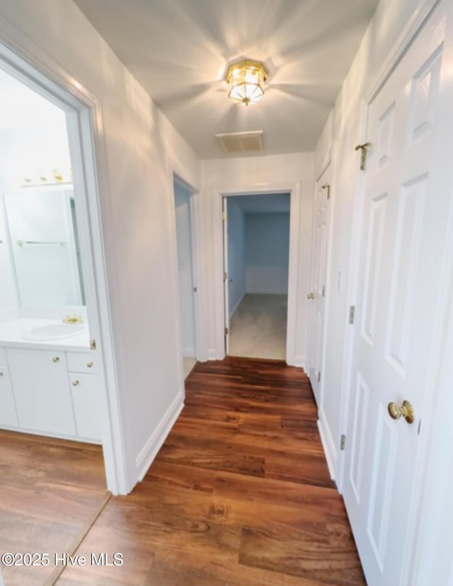 hall featuring a sink, wood finished floors, visible vents, and baseboards