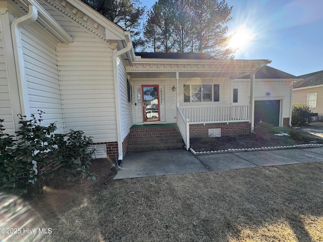 entrance to property featuring covered porch, crawl space, and a garage