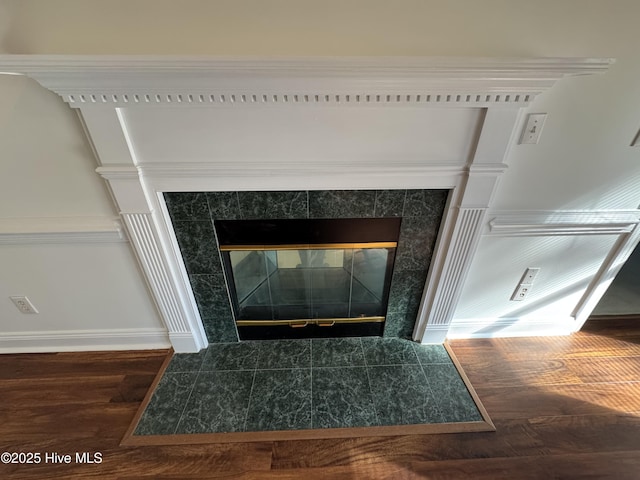 room details with baseboards, a tiled fireplace, and wood finished floors