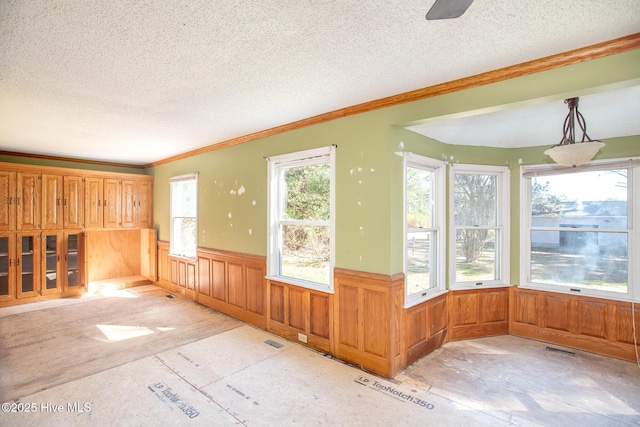 empty room with visible vents, a textured ceiling, ornamental molding, and wainscoting