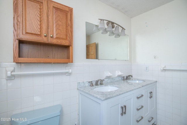 bathroom featuring a sink, toilet, a wainscoted wall, and a textured ceiling