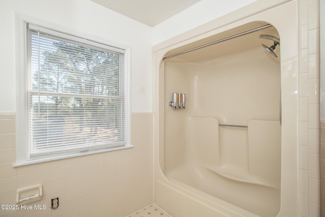 full bath with a tub, a textured ceiling, tile walls, wainscoting, and a shower