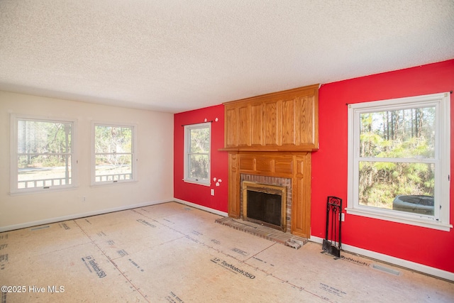 unfurnished living room featuring a brick fireplace, a textured ceiling, and baseboards