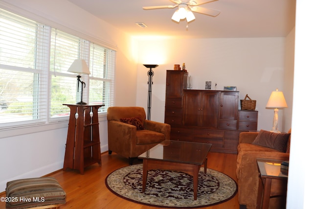 living area featuring ceiling fan, wood finished floors, visible vents, and baseboards