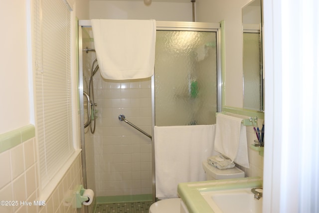 bathroom with a shower with shower door, a sink, tile walls, and toilet