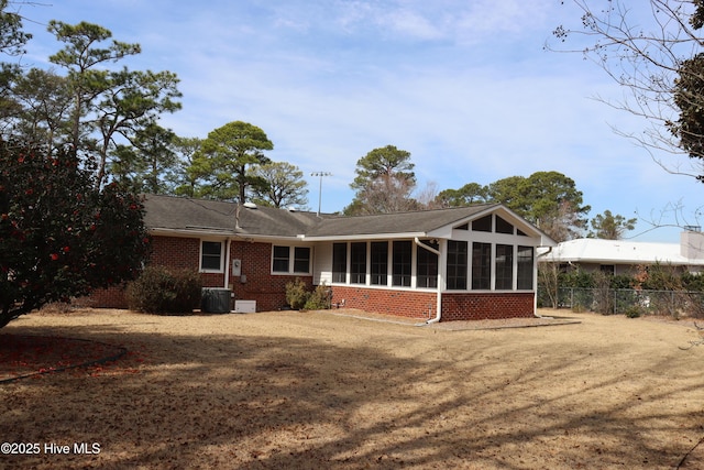 rear view of house with brick siding, central air condition unit, a lawn, a sunroom, and fence