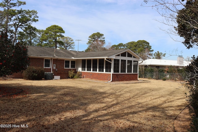 rear view of house with central AC unit, a sunroom, fence, a yard, and brick siding