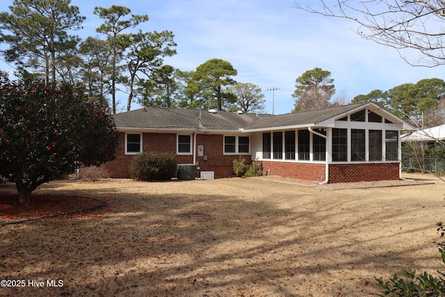 back of property with central AC, brick siding, a lawn, and a sunroom