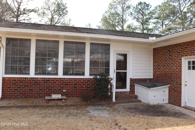 entrance to property with a patio area, a shingled roof, and brick siding