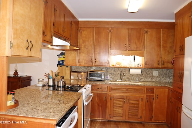 kitchen with light stone counters, white appliances, a sink, backsplash, and brown cabinets